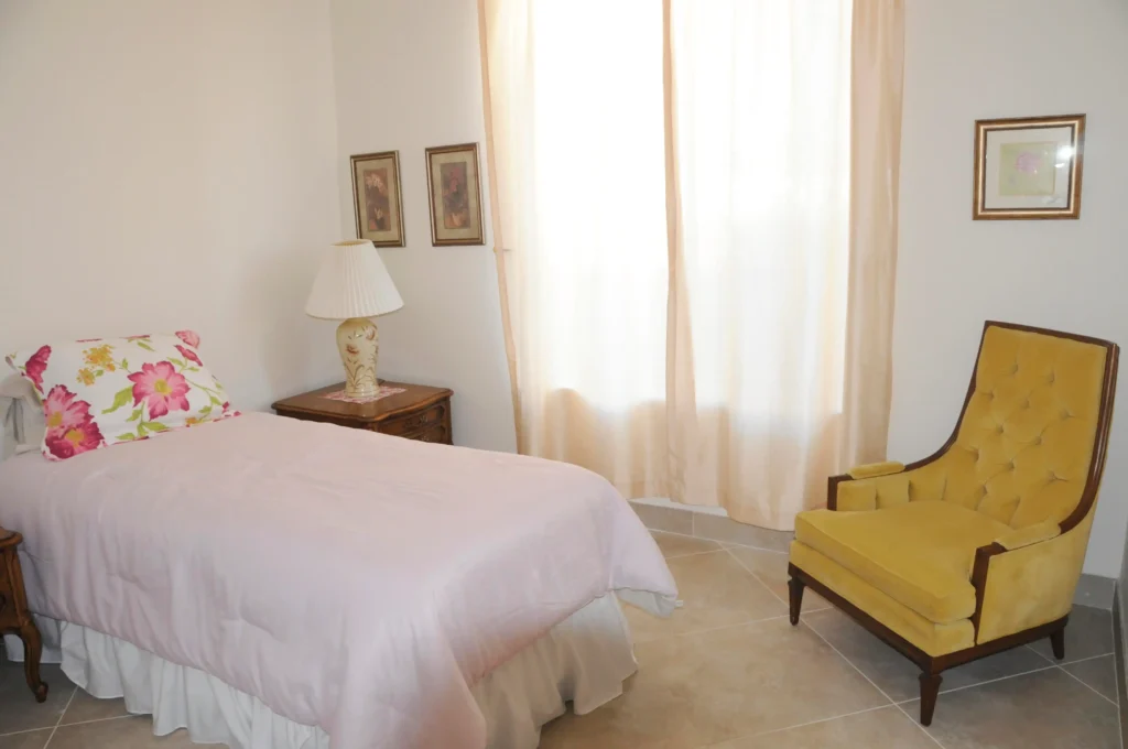 A bedroom with a bed and chair in an Alzheimer's care community.